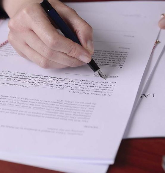 Mano sosteniendo un bolígrafo, firmando un documento sobre una pila de papeles blancos.