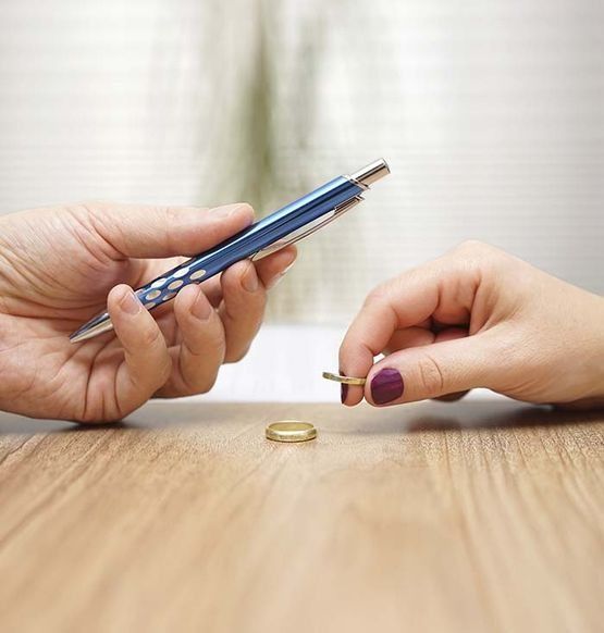 Unas manos intercambian un anillo de boda y un bolígrafo sobre una mesa de madera, lo que sugiere un divorcio.