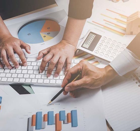 Manos trabajando en un teclado y señalando gráficos con una calculadora, lo que indica una reunión de negocios.