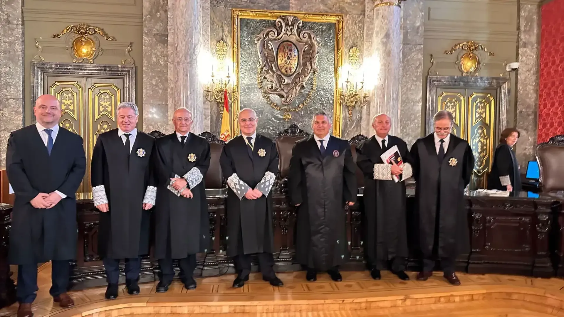 Grupo de hombres con togas judiciales posando en una sala de audiencias con detalles ornamentados.