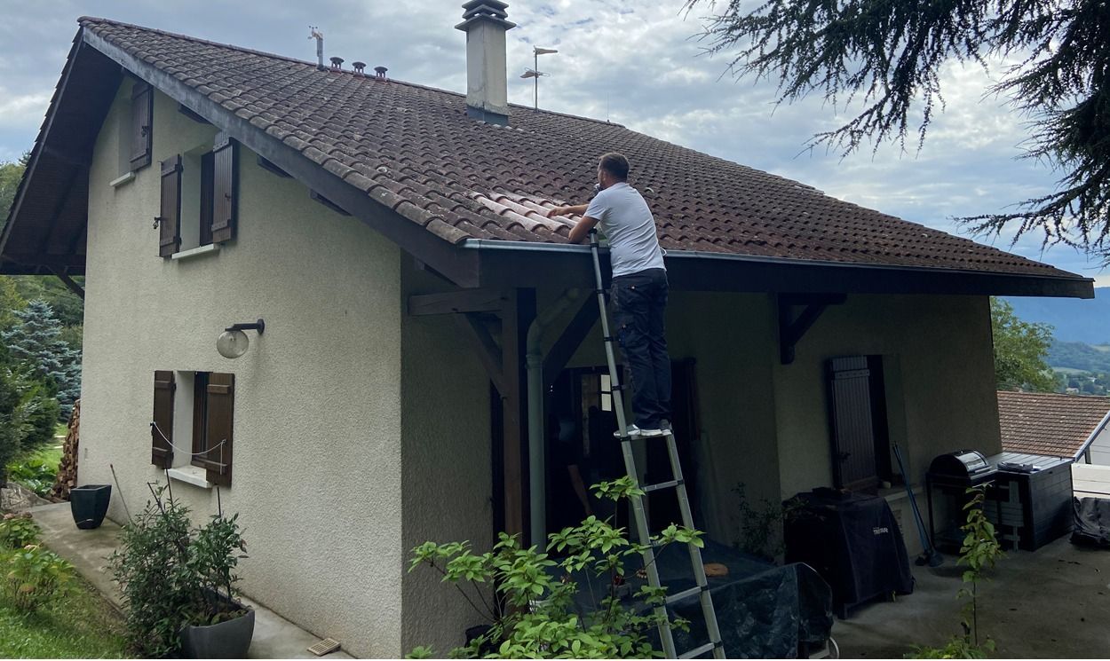 Une personne sur une échelle en train de manipuler une tuile sur une toiture.