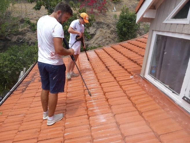 Deux personnes en train de nettoyer une toiture au jet à haute pression.