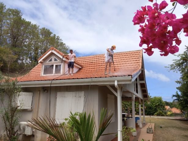 Deux personnes sur un toit en train de nettoyer les tuiles à l'aide de pistolets à eau à haute pression.