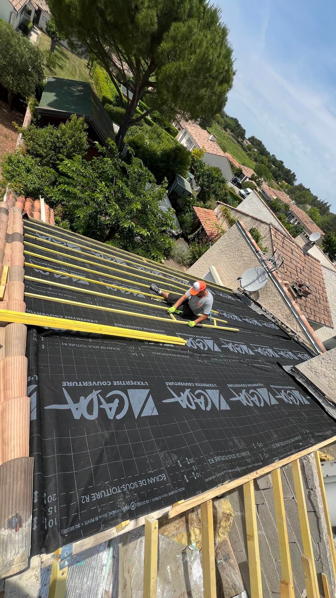 Un homme assis en train de placer des tiges de bois sur une toiture en cours de rénovation.