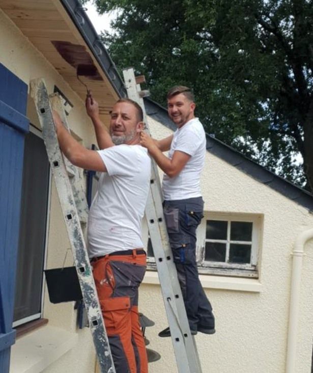 Deux personnes souriantes sur leurs échelles en train de regarder l'objectif.