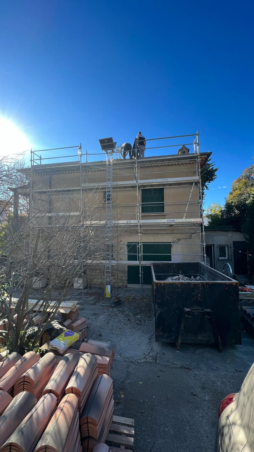 Échafaudage contre la façade d'une maison où des artisans sont présents sur la toiture.