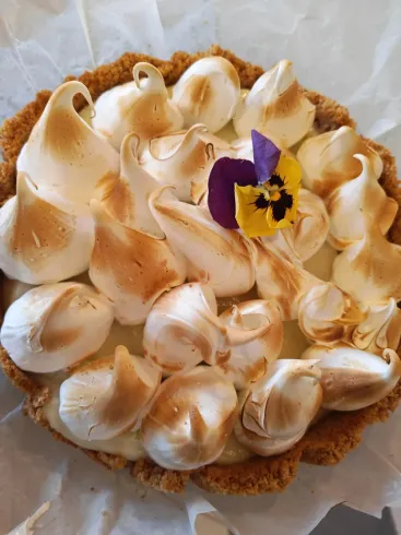 Pastel blanco glaseado con espirales de merengue tostado y una pequeña flor comestible morada encima.