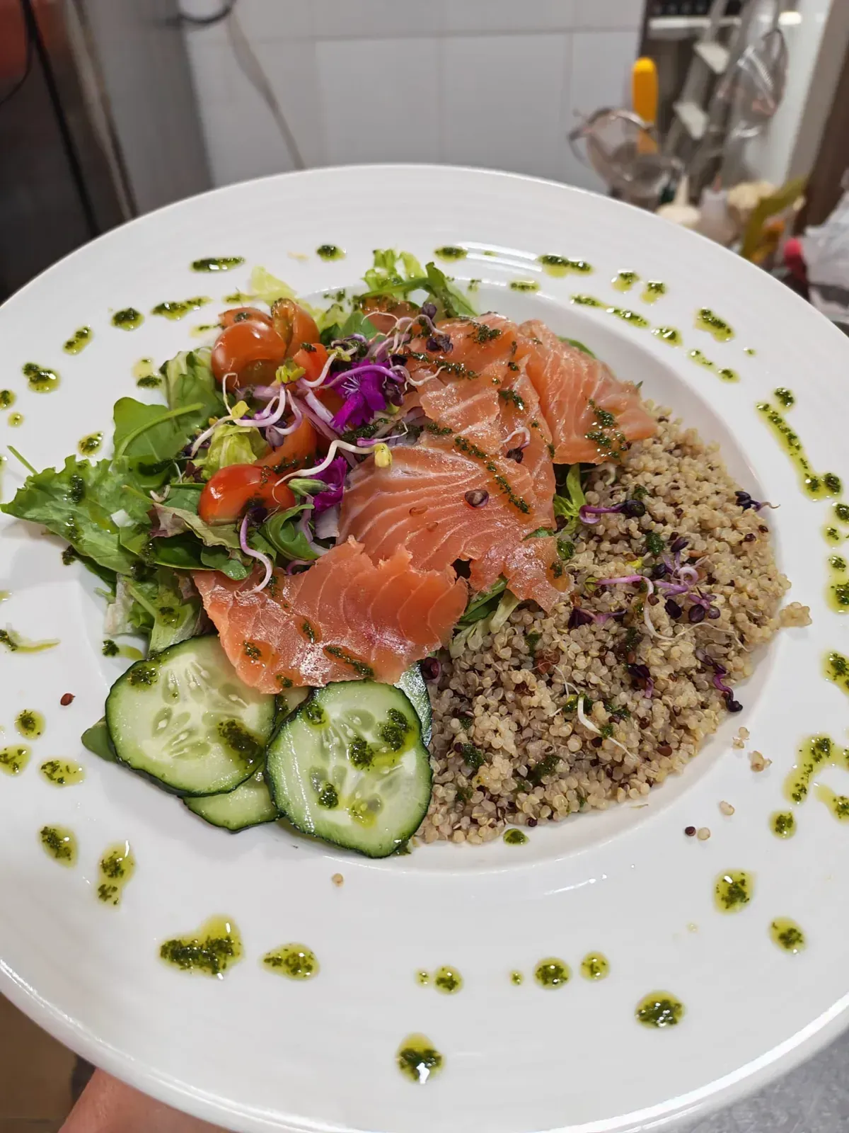 Ensalada de salmón con quinoa, pepinos, tomates, verduras y aceite de hierbas en un plato blanco.