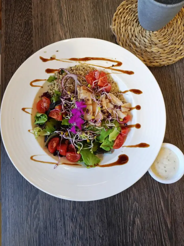 Ensalada con verduras, fresas, nueces y salsa rociada en un plato blanco junto a una bebida en una mesa.