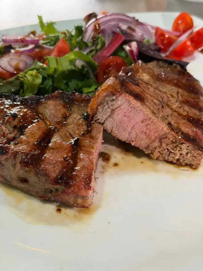 Filete a la parrilla en rodajas con ensalada en un plato blanco.