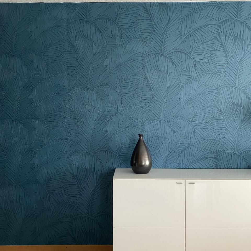 Un vase est posé sur une commode devant un mur bleu.