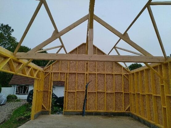 Ossature en bois d'un bâtiment en construction; vue intérieure avec chevrons apparents, revêtement OSB et porte.