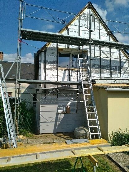 Échafaudage installé à l'extérieur d'une maison en construction ; murs blancs et gris ; ciel bleu vif.