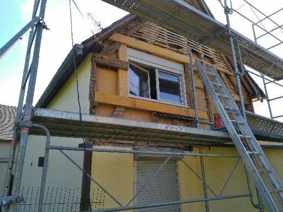 Maison en rénovation avec échafaudage, fenêtre apparente et charpente apparente.