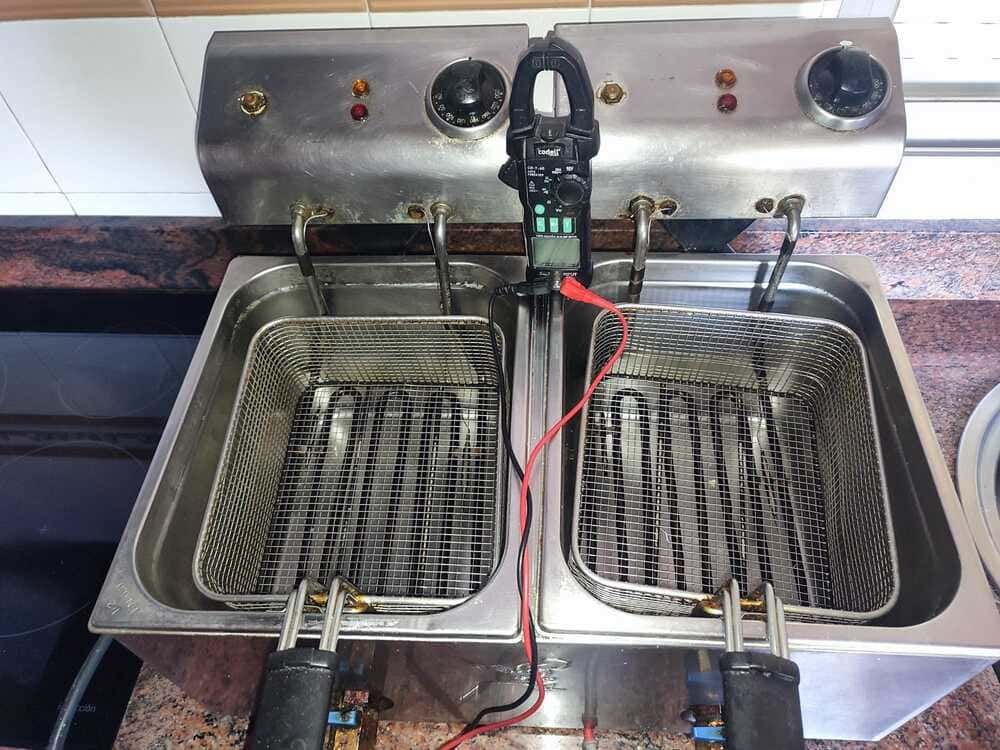 Freidora abierta con dos cestas y un termómetro de sonda en el centro.