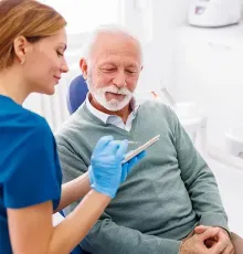 Un anciano está sentado en una silla dental hablando con una enfermera.