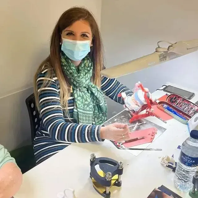 Una mujer que lleva una máscara está sentada en una mesa con un modelo dental.