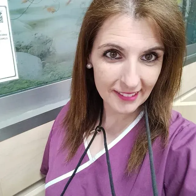 Una mujer con un uniforme morado se toma una selfie con un estetoscopio alrededor del cuello.