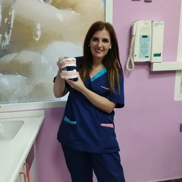 Una mujer con un uniforme azul sostiene un modelo de dientes.