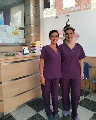 Dos mujeres con uniformes morados están paradas una al lado de la otra en una habitación.