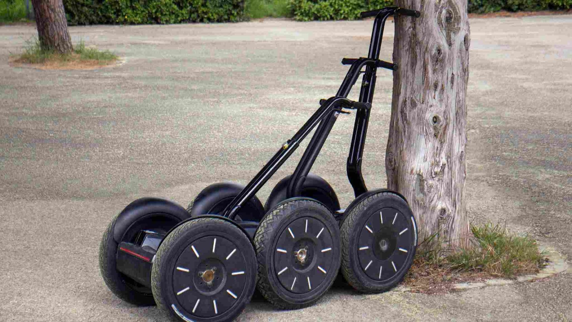 Transportador personal negro de varias ruedas, apoyado contra un árbol, al aire libre.