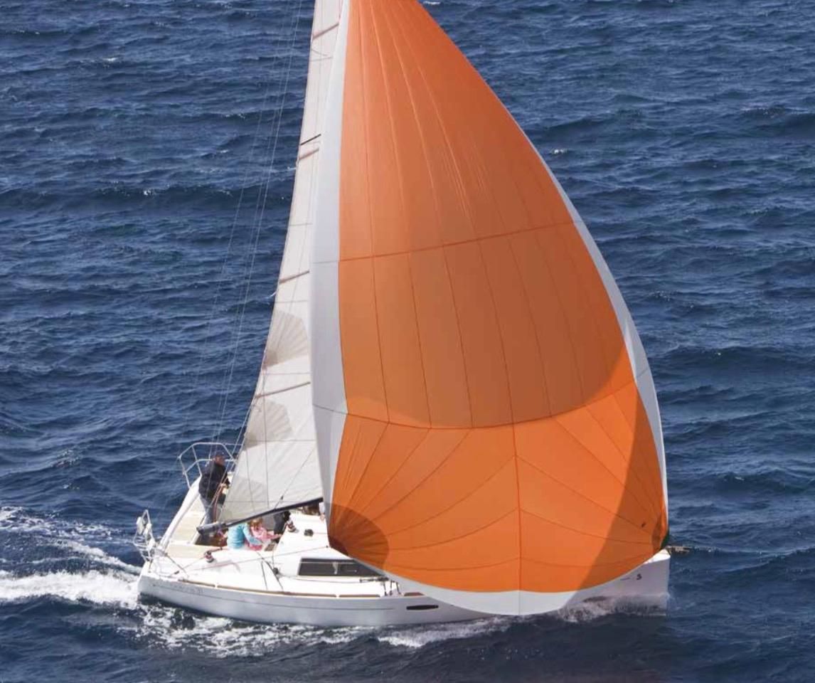 Velero blanco con una gran vela naranja surcando las aguas azules agitadas.