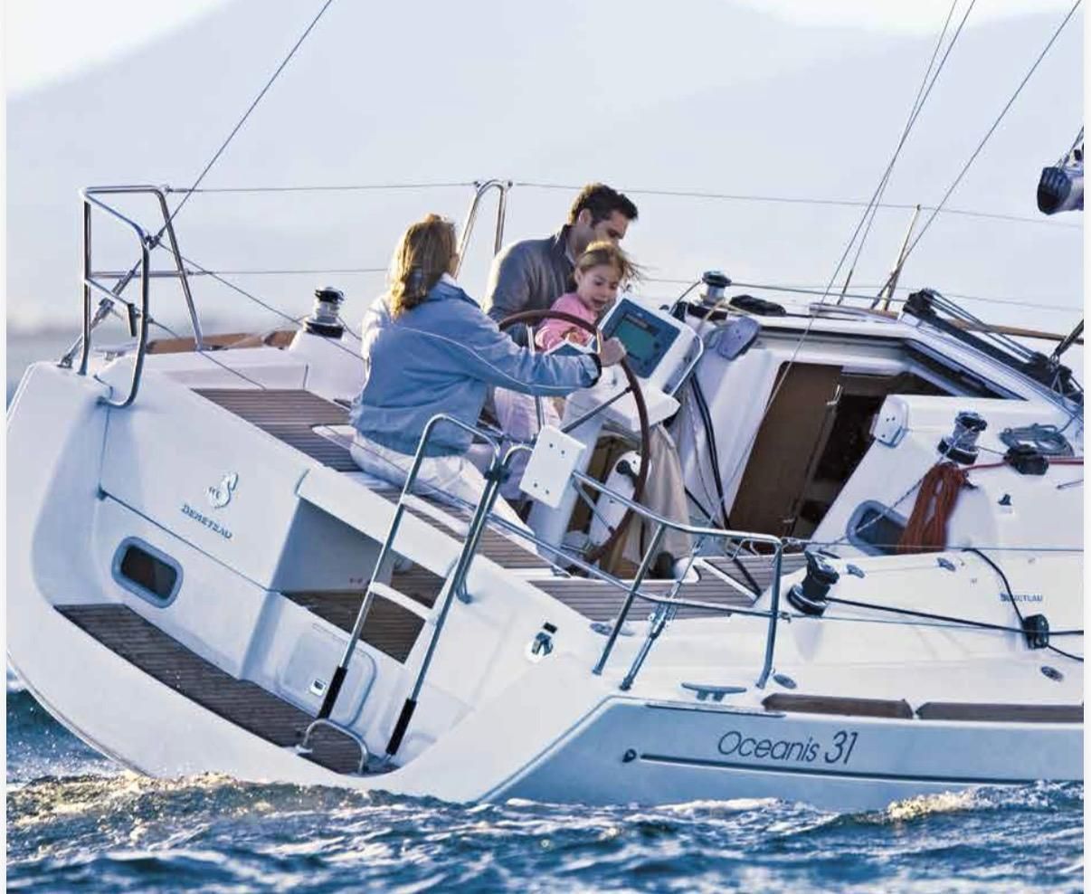 Gente navegando en un velero blanco llamado Océanis 31 en aguas agitadas.