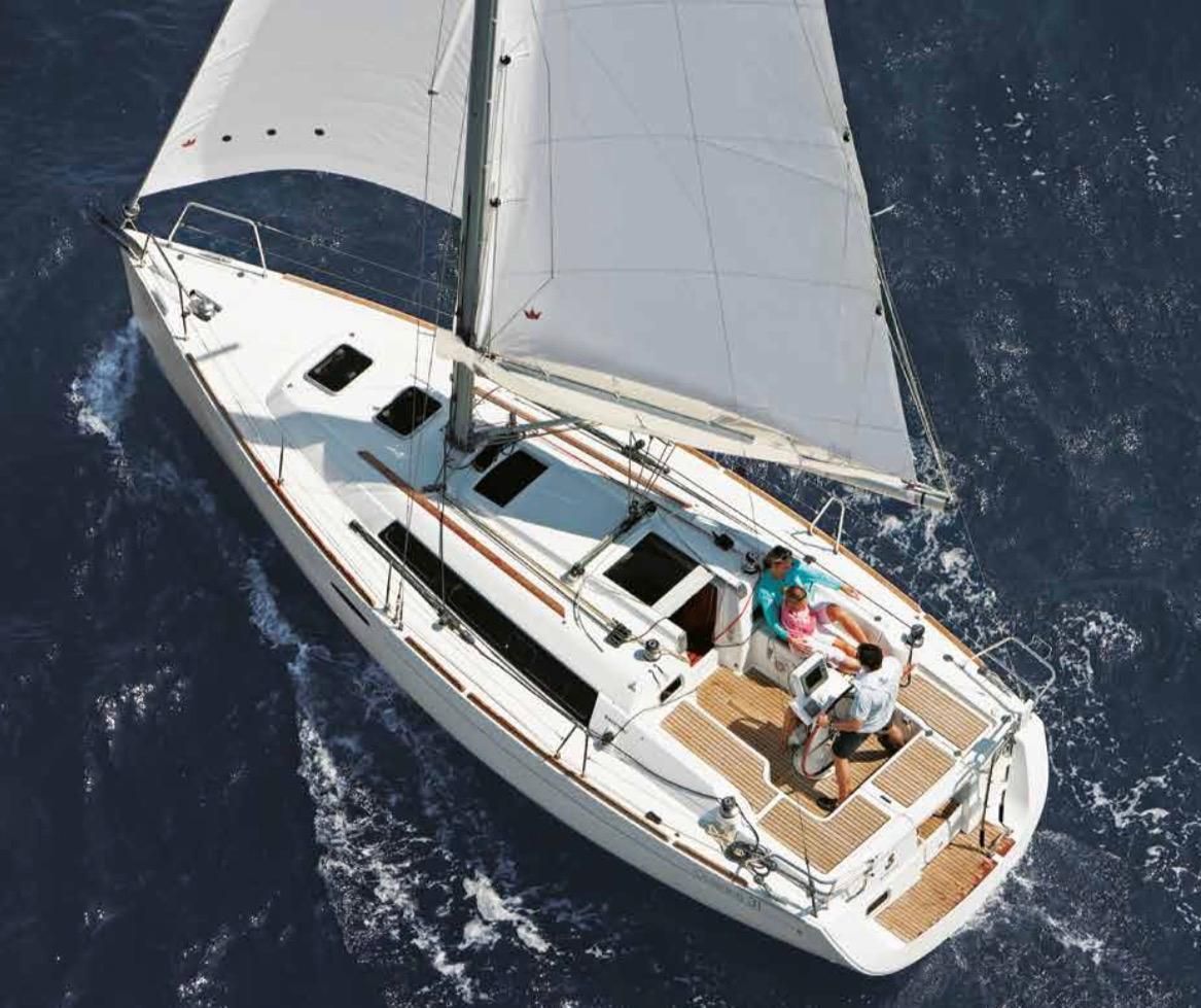 Un velero blanco con las velas desplegadas, navegando sobre aguas abiertas de color azul oscuro con algunas personas en cubierta.