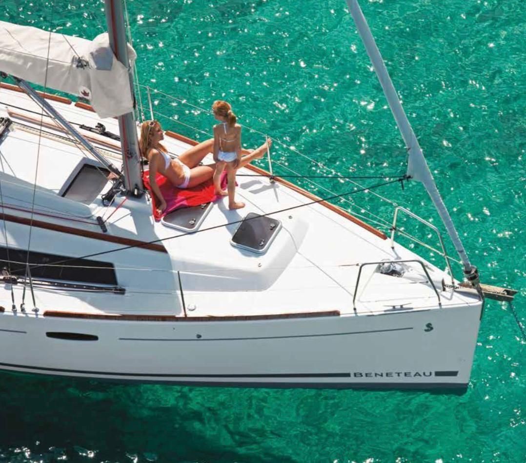 Dos personas se relajan en un velero blanco en aguas turquesas.