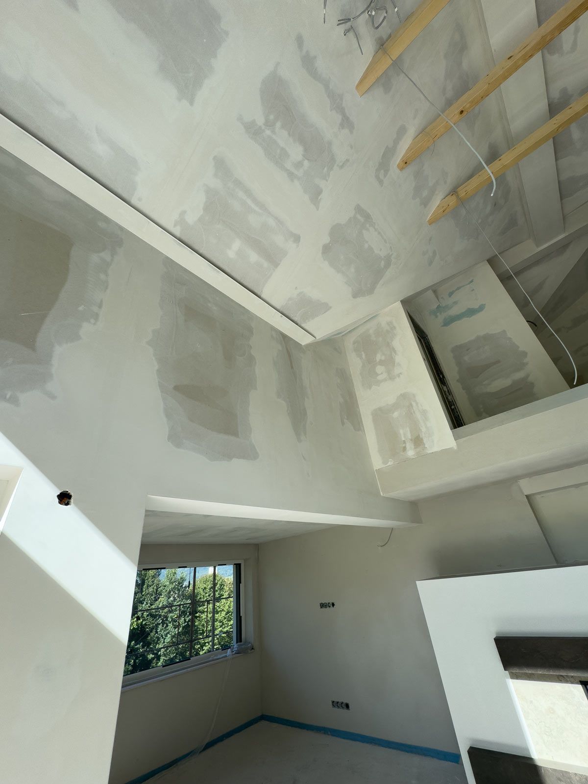 Innenraum im Umbau mit unfertigen Trockenbauwänden, einem Fenster und freiliegenden Deckenbalken.