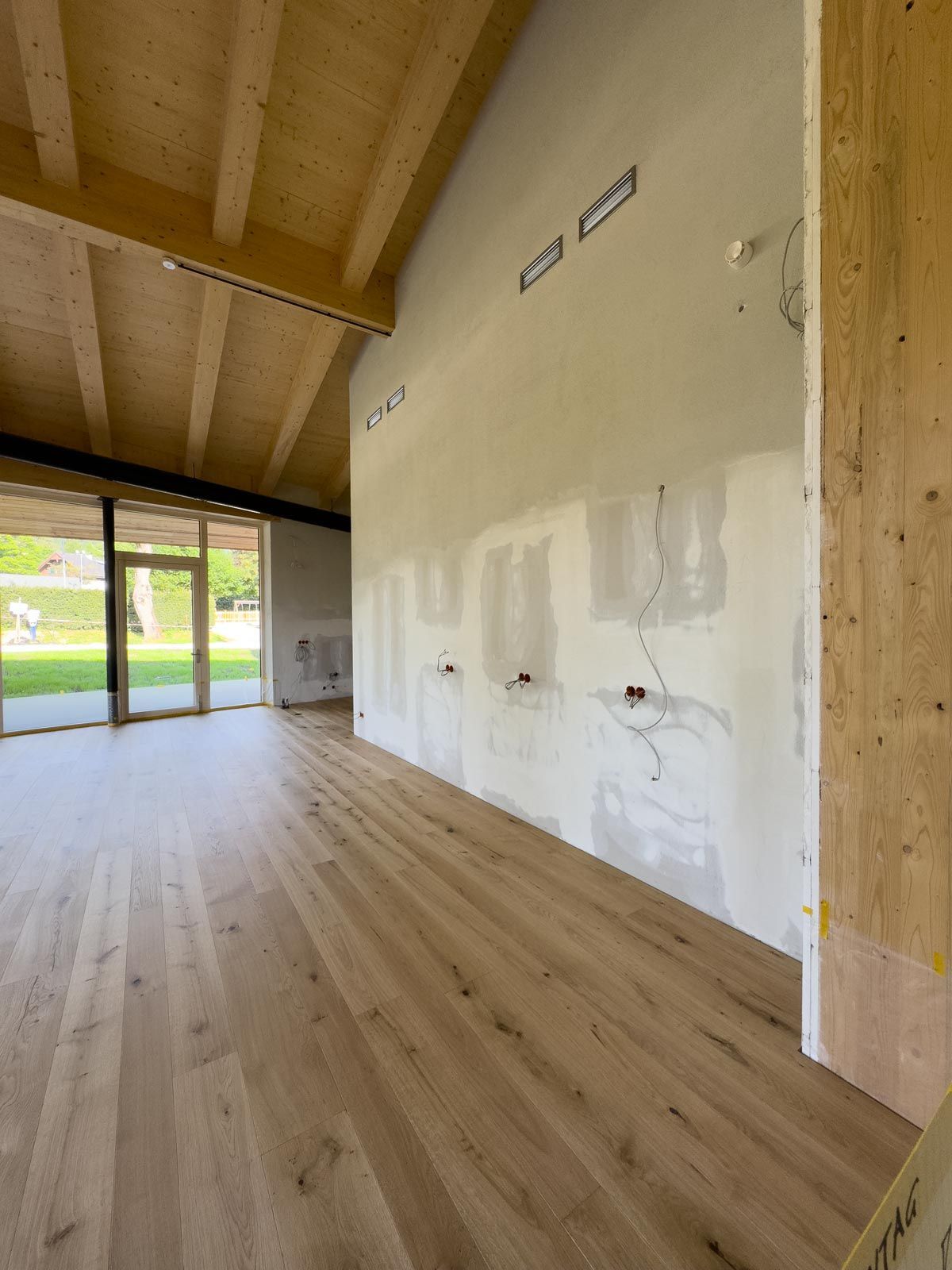 Leeres, modernes Zimmer mit hellem Holzboden, hoher Holzdecke und großen Glasschiebetüren.