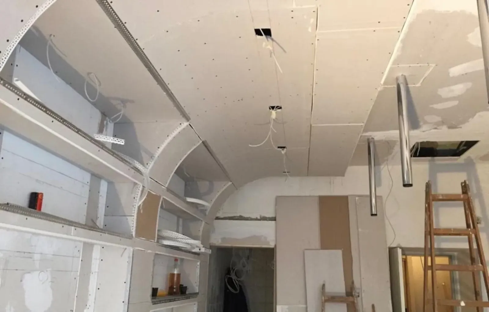 Innenraum im Umbau mit freiliegenden Gipskartonwänden, ausgebesserter Decke, Regalen und einer Leiter.