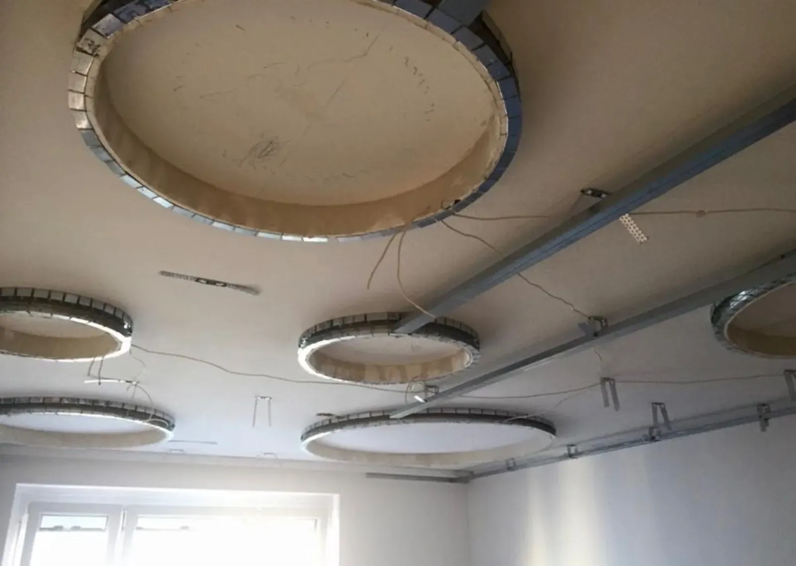 Die Decke in einem Raum befindet sich im Bau und ist mit runden Einbauleuchten und freiliegenden Kabeln ausgestattet.