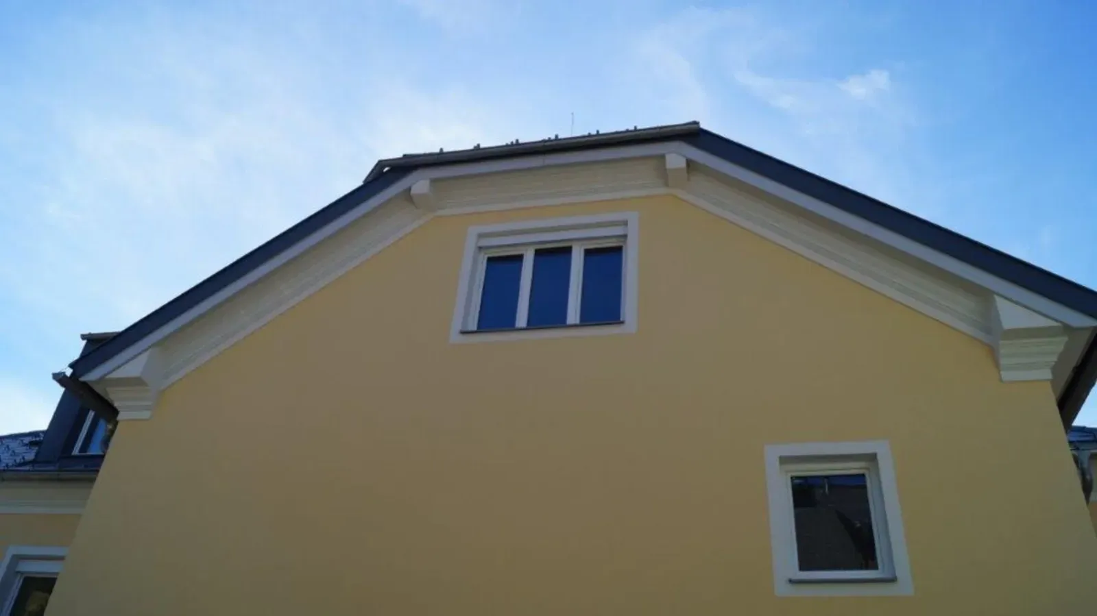 Gelbe Hausfassade mit zwei Fenstern auf einem schrägen Dach