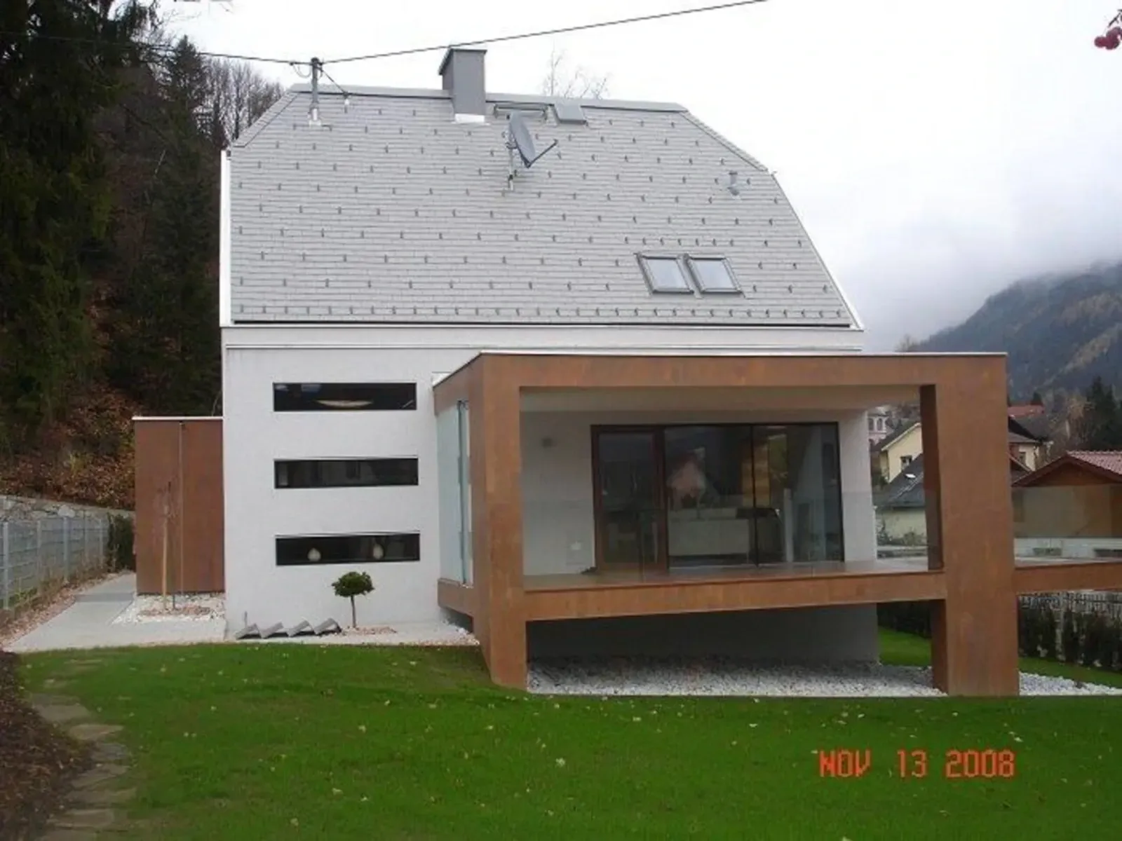 Modernes Haus mit großem, holzgerahmtem Glasanbau und schrägem, weißem Dach auf einem grasbewachsenen Grundstück