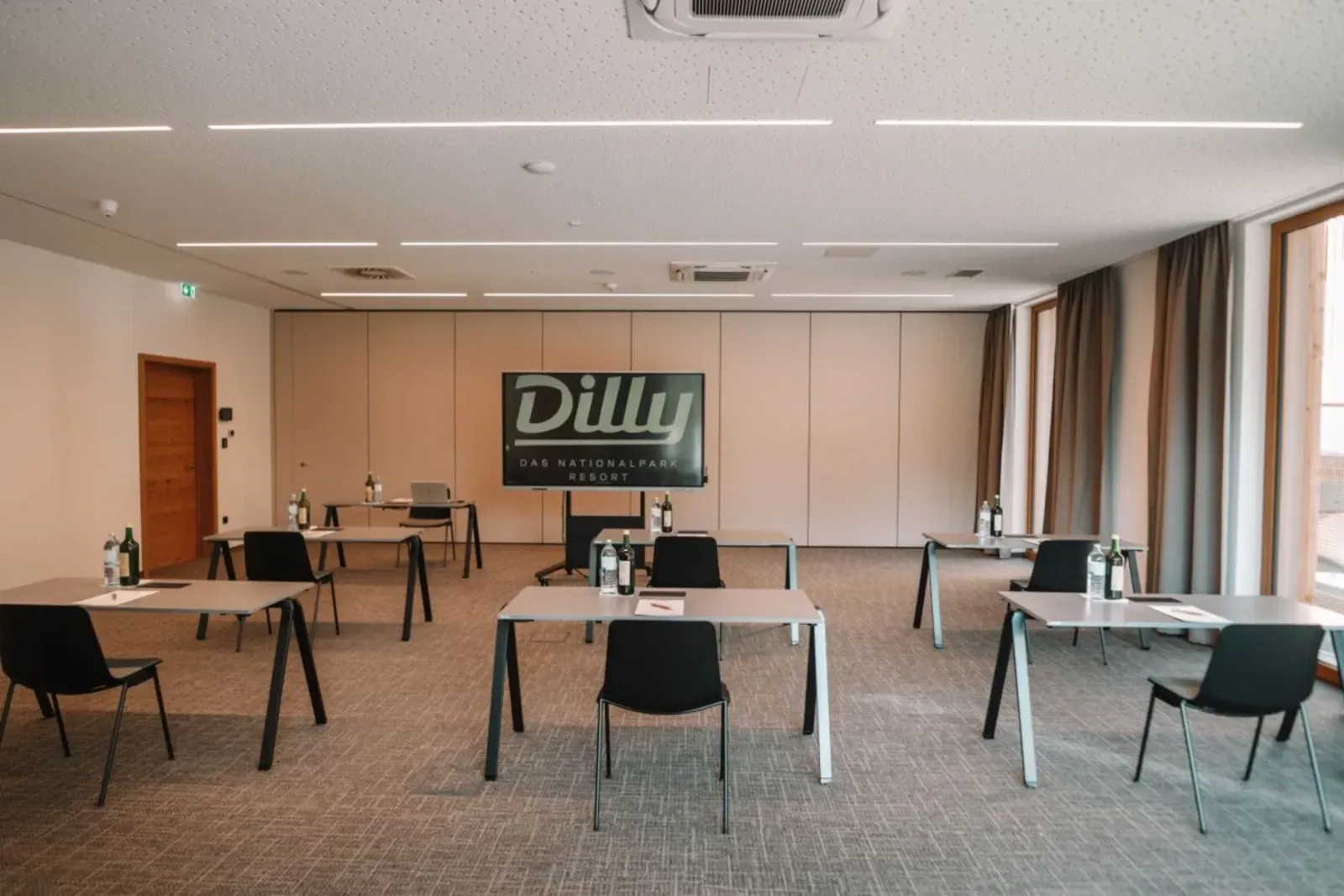 Leerer Konferenzraum mit Tischen und Stühlen, großem Wandschild und Teppichboden.