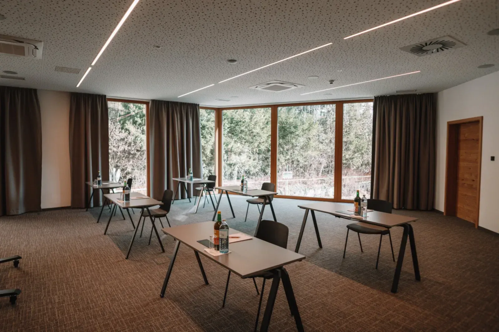 Leerer Konferenzraum mit Tischen und Stühlen, großen Fenstern, Vorhängen und Teppichboden