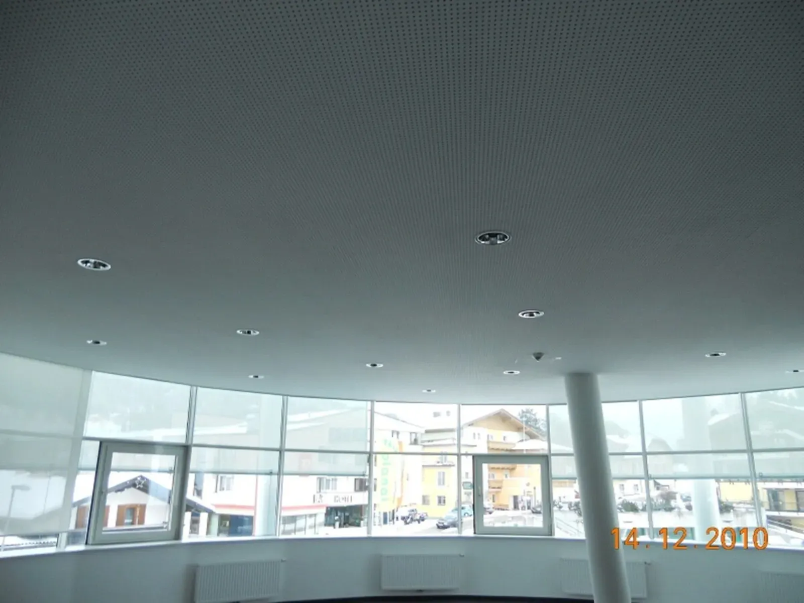 Großzügige, moderne Lobby mit gebogenen Glasfenstern, grauer Decke und hellem Ausblick nach draußen.