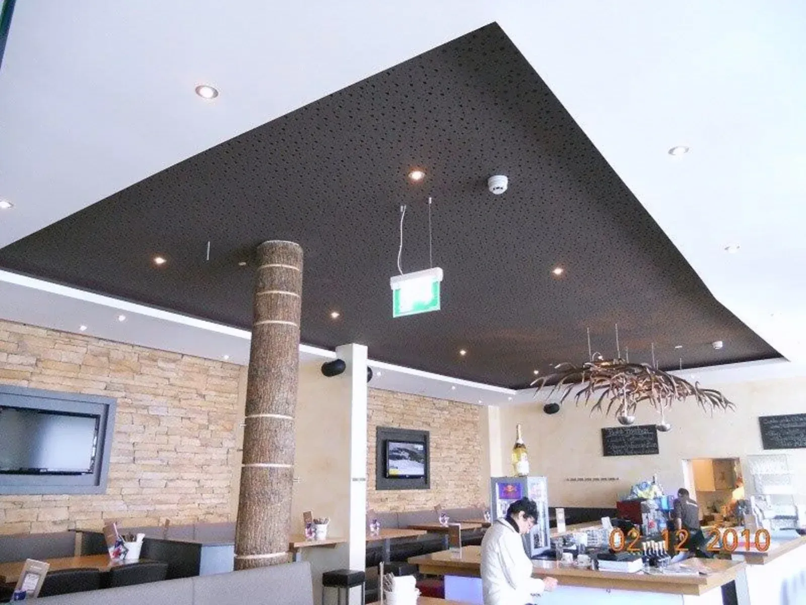 Modernes Café-Interieur mit schwarzer Decke, Steinwand und Sitzgelegenheiten an der Theke, mit einem Mitarbeiter hinter der Bar.