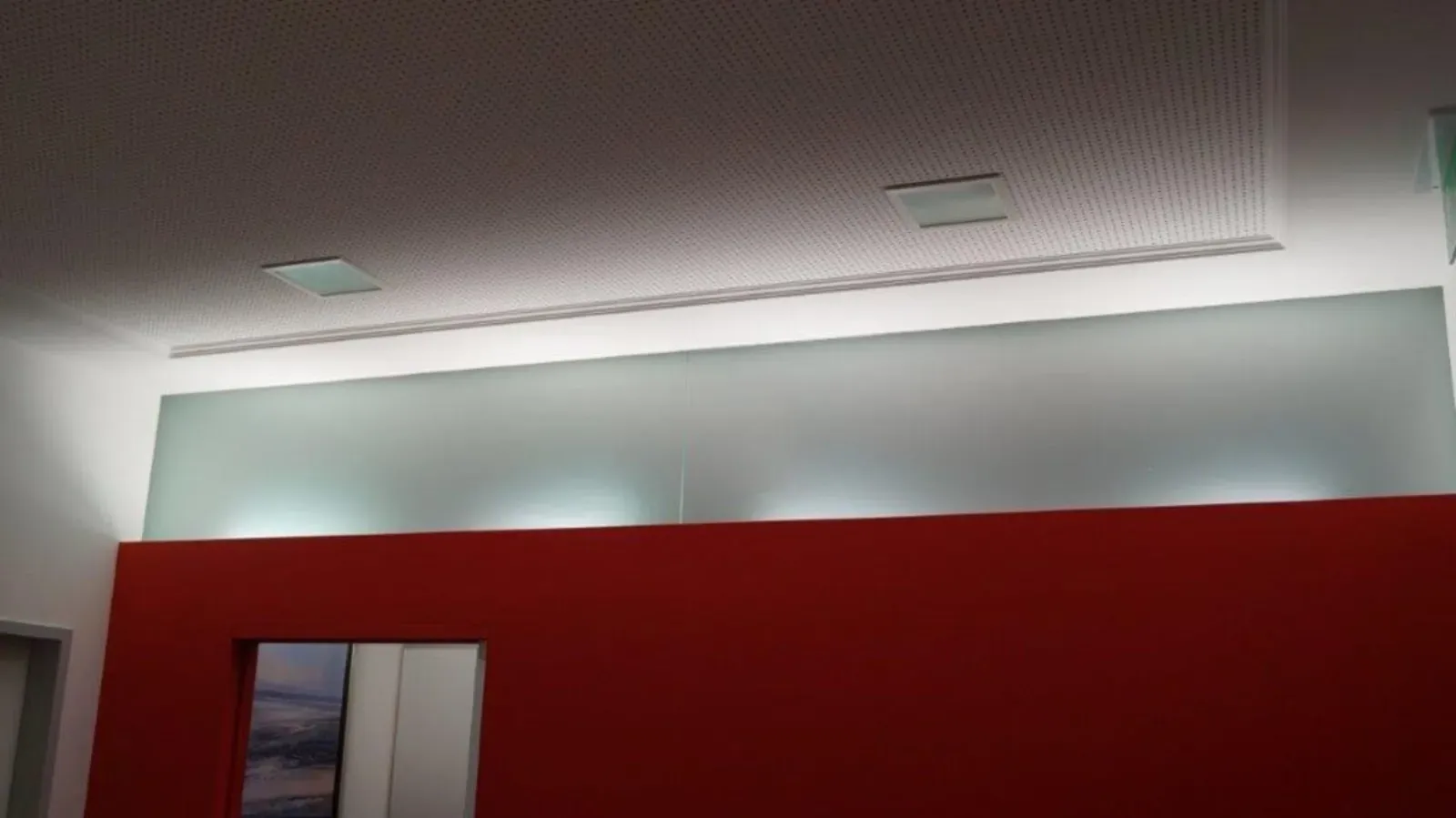 Innenbereich mit roter Wand, Milchglasscheibe und weißen Deckenleuchten.