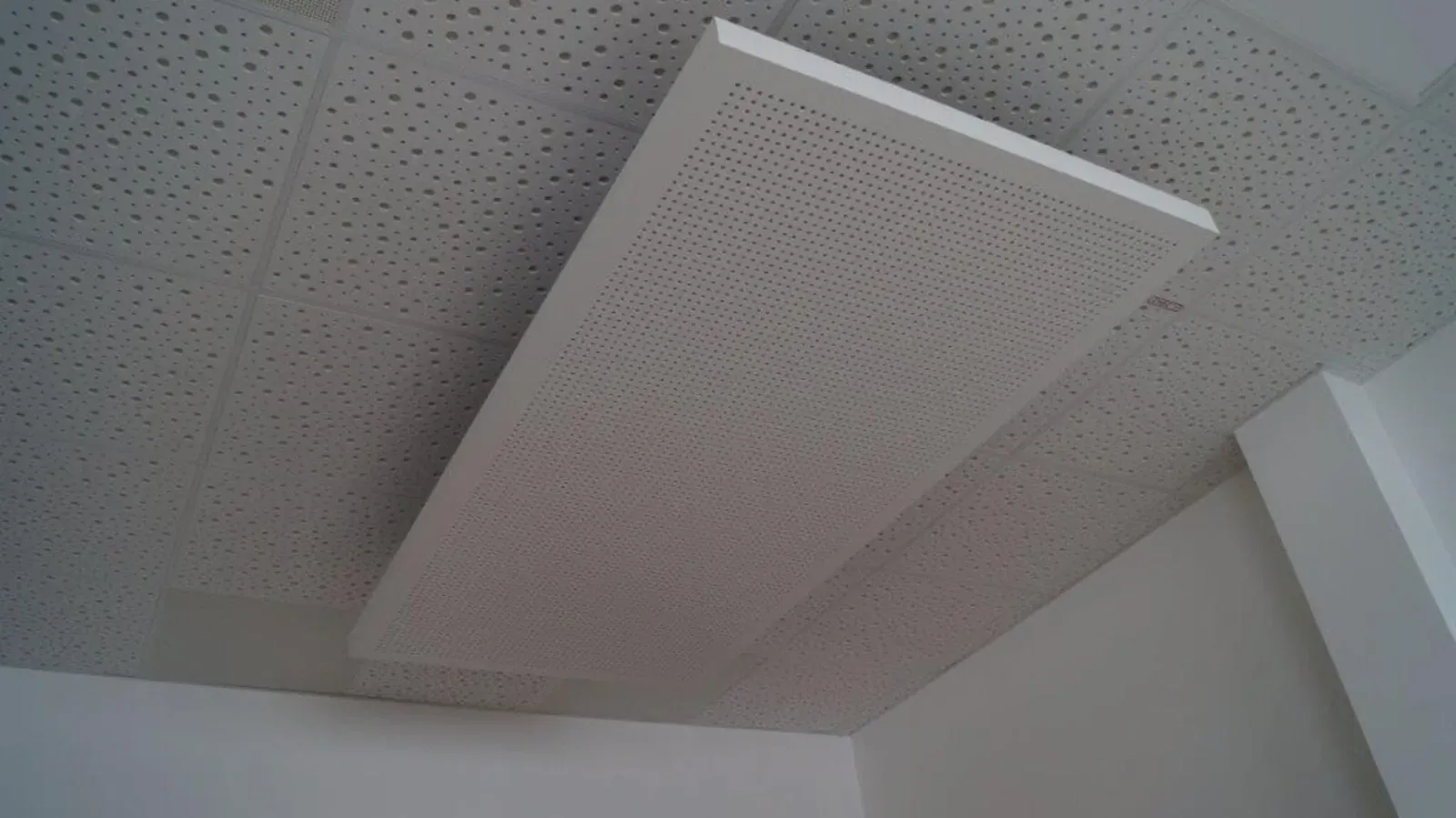 Weiße Akustikdeckenplatte, die in einer Ecke eines Raumes an einer perforierten Decke montiert ist