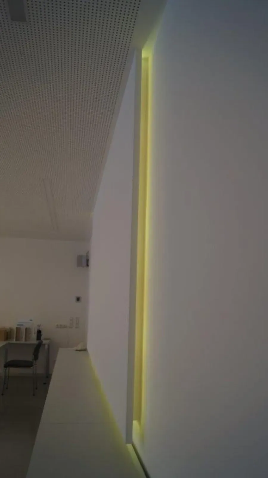 Moderner Flur mit einem vertikalen gelben LED-Lichtstreifen an einer weißen Wand