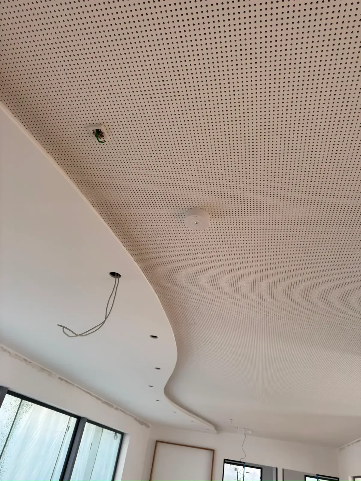 Abgehängte Decke mit perforierten Paneelen und herabhängenden Stromleitungen in einem Raum, der renoviert wird