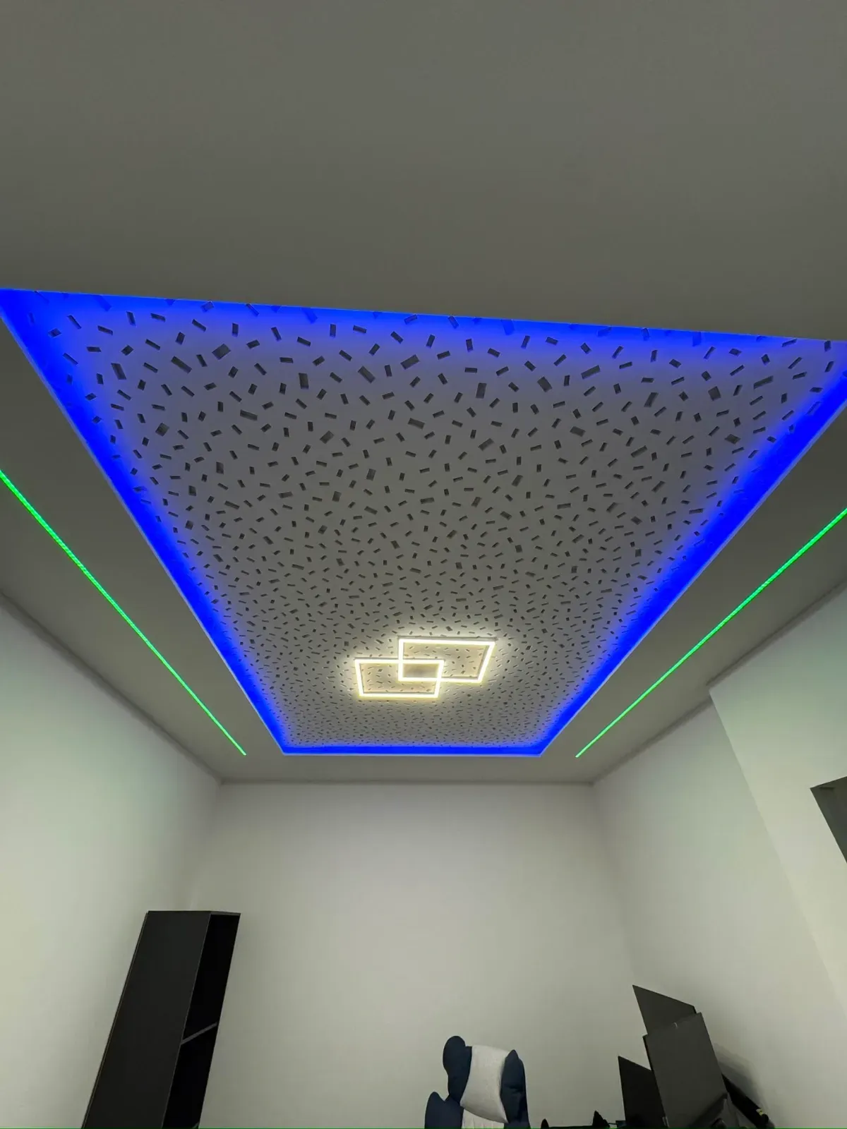 Moderne Zimmerdecke mit blauem LED-Rand, sternenförmigem Lochpaneel und geometrischem Kronleuchter über weißen Wänden