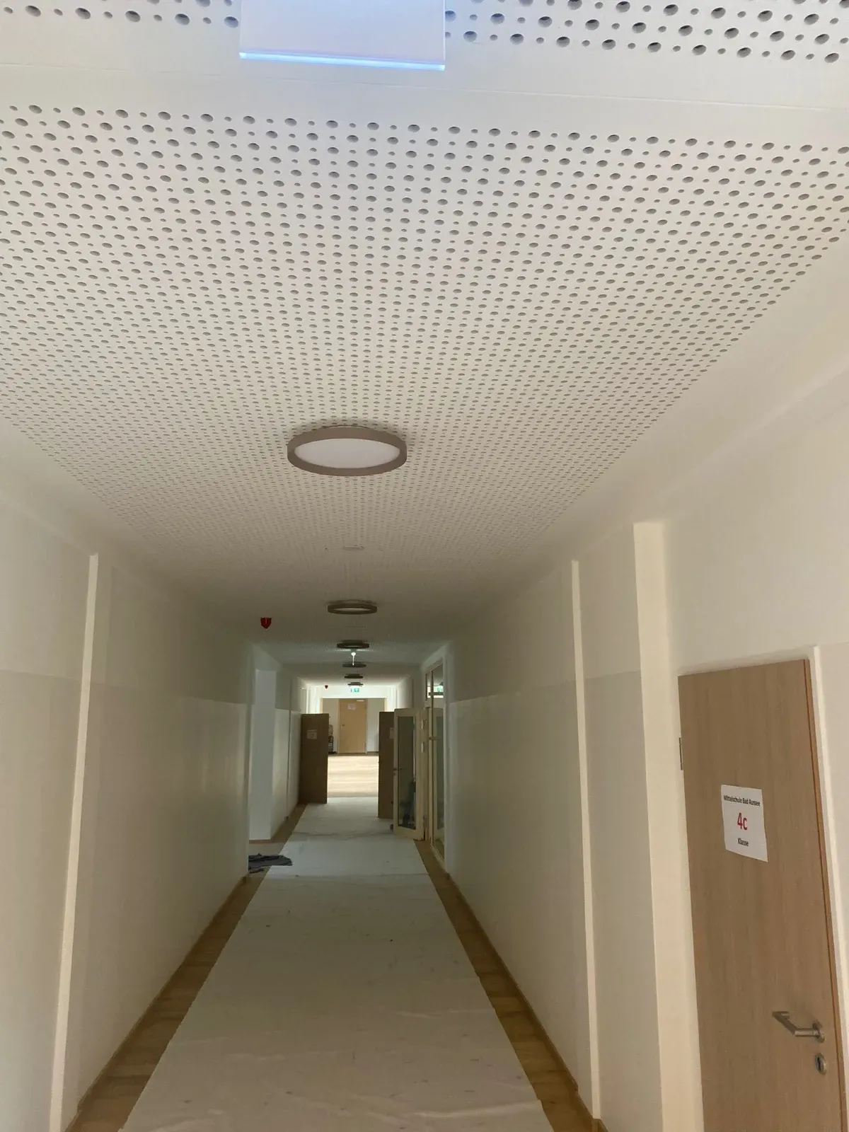 Leerer beigefarbener Flur mit gemusterter Decke, runder Deckenleuchte und Türen an den Seiten.