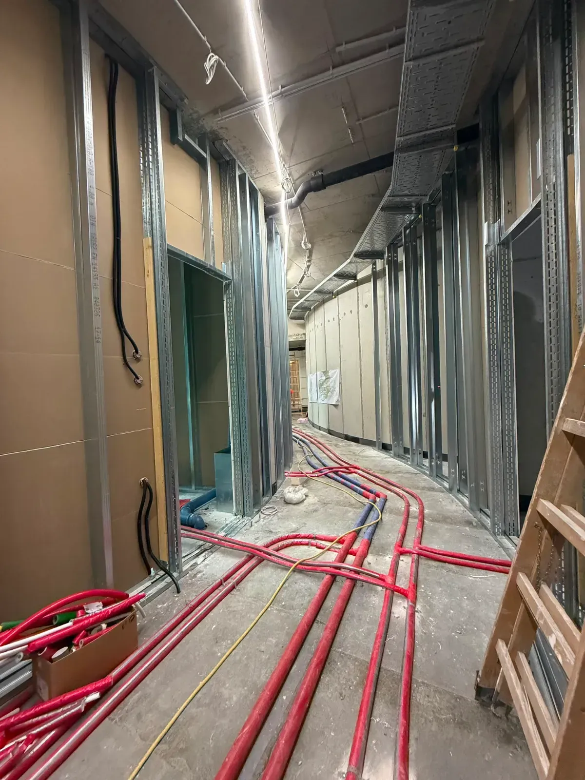 Teilweise fertiggestellter Flur mit roten Elektroleitungen und freiliegenden Wänden auf einer Baustelle