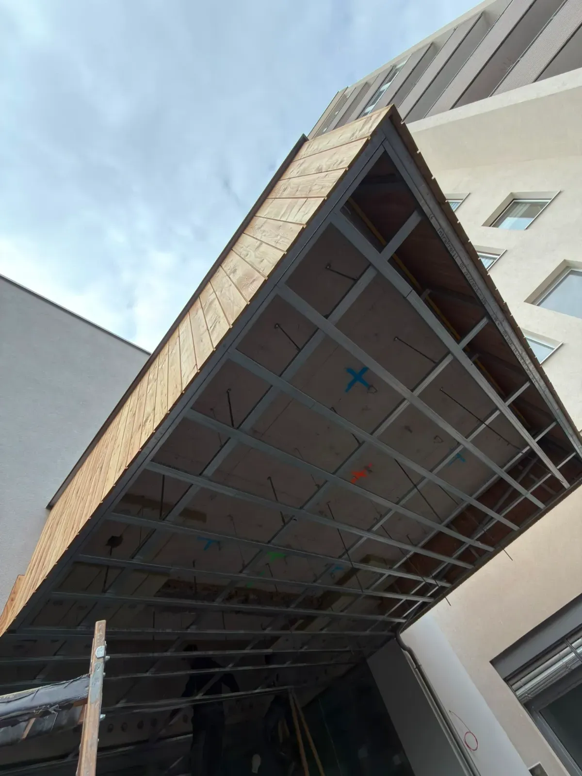 Überdachter, im Bau befindlicher Gehweg neben einem Gebäude, von unten vor dem Himmel betrachtet.