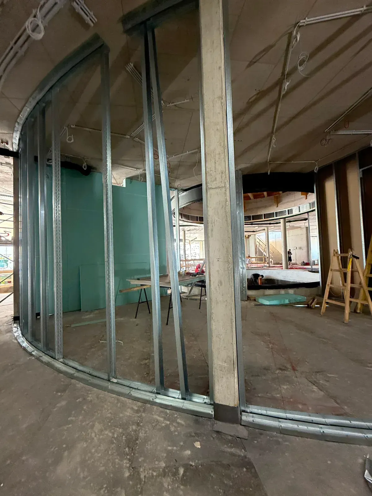 Gebogene, mit Glas umrahmte Konstruktionswand in einem unfertigen Gebäude, mit freiliegenden Ständern und Betonboden.