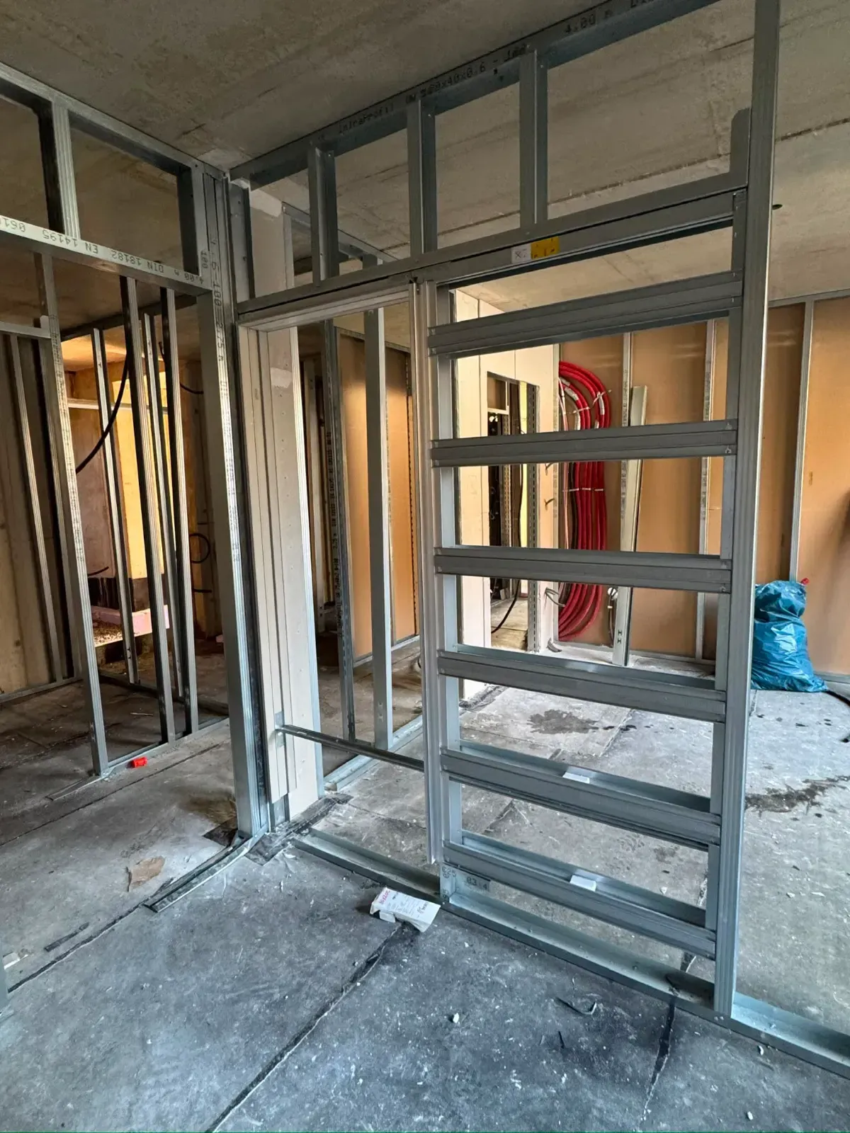 Metallwandkonstruktion in einem unfertigen Innenraum mit freiliegendem Betonboden und roter Feuerwehrschlauchhaspel.