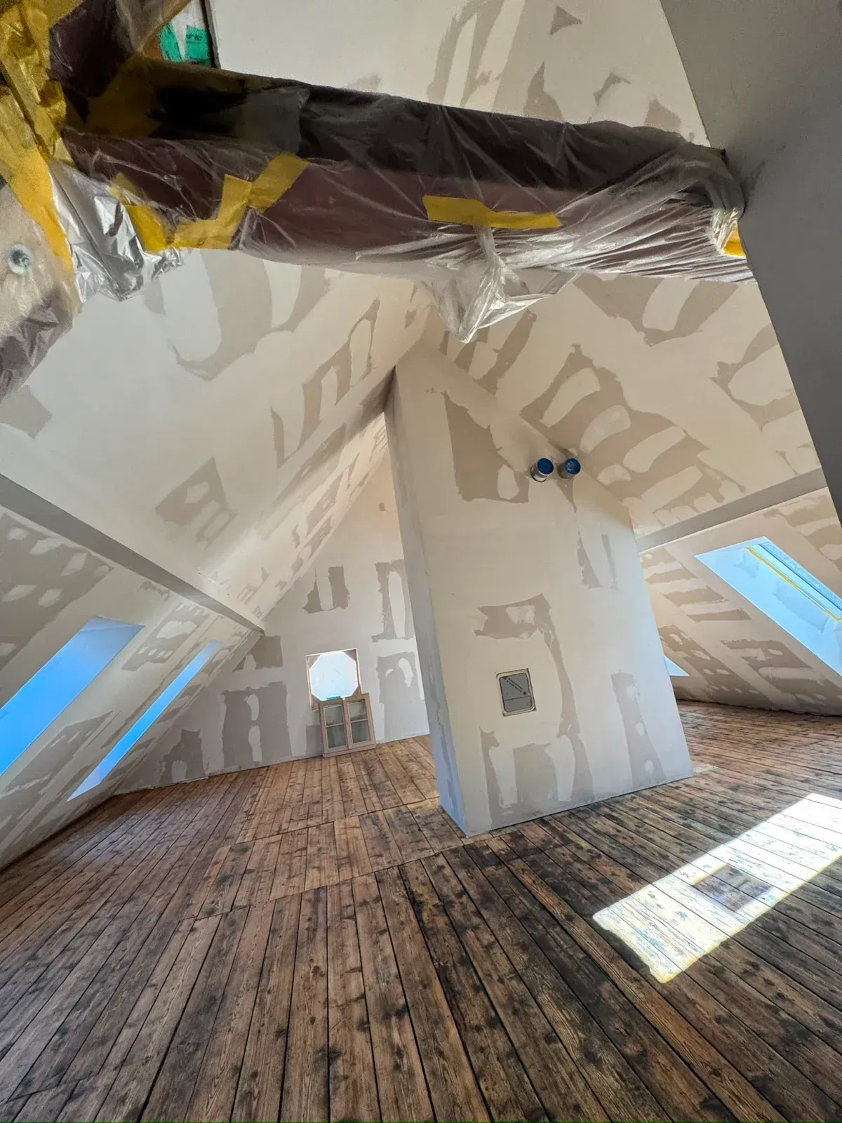 Dachzimmer mit schrägen Wänden, freiliegenden Balken und unfertigem Holzboden im Bau